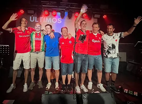 La banda con camisetas de fútbol sobre el escenario, los brazos en alto y su nombre en el muro de luz.