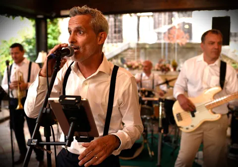 El cantante al micrófono en una terraza, con el trombón y el bajo detrás.