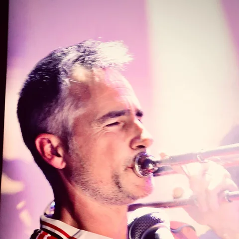Arnaud toca el trombón en primer plano, con el micrófono delante.