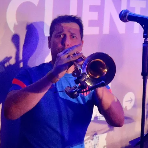 Guillaume toca la trompeta en escena, bajo luz azul y violeta.
