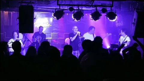 La banda al completo en el escenario de Rockville, la sala llena de siluetas.