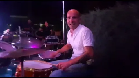 El batería sonriendo detrás de la batería en un concierto al aire libre.