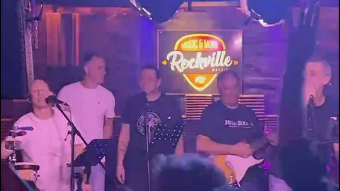Últimos Clientes cantando ante el rótulo luminoso de Rockville, Madrid.