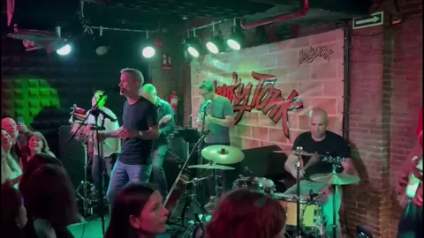 Siete músicos tocando en un bar de ladrillo visto, con el público muy cerca.